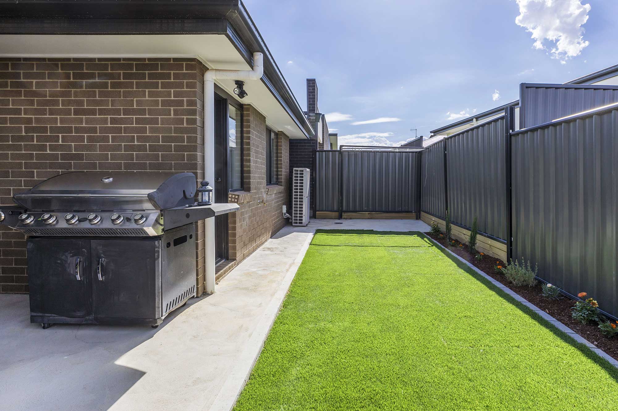 Side yard with turf and built-in BBQ area at a custom home build in Taylor, Canberra completed by CanDo House.