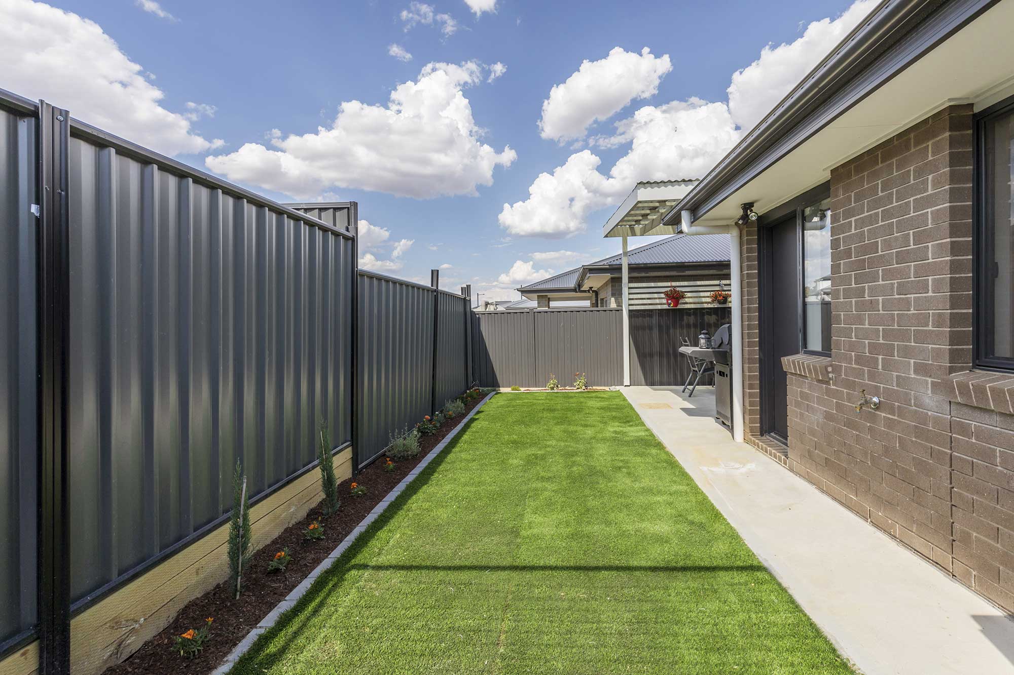 Landscaped side yard with fresh turf, garden beds and fencing at a custom home build in Taylor, Canberra by CanDo House.